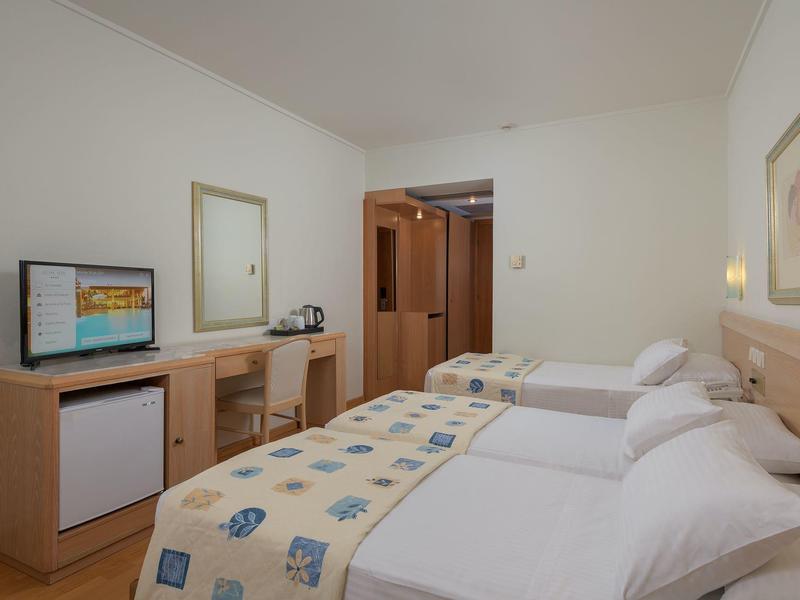 Una camera d'hotel con due letti singoli, scrivania, sedia, specchio e piccolo frigorifero.