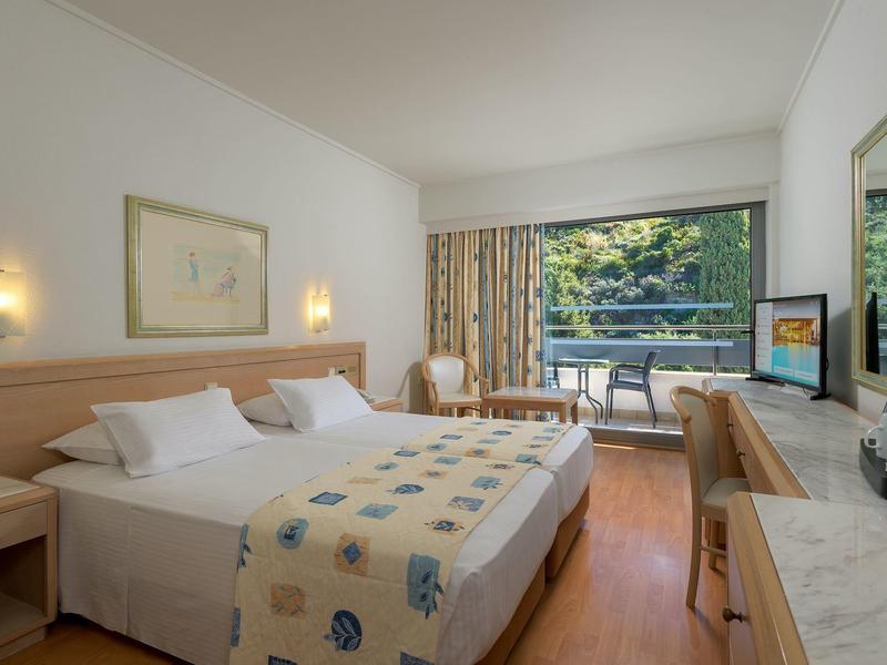 Camera d'hotel luminosa con letto matrimoniale, balcone, zona salotto e arredo moderno.