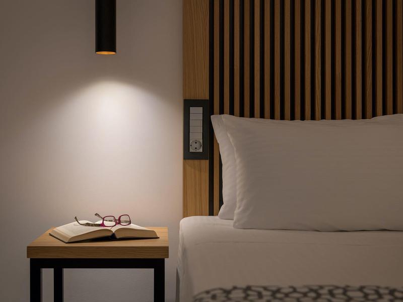 Semplice scena del comodino con libro, occhiali e lampada da comodino in una camera d'hotel moderna.