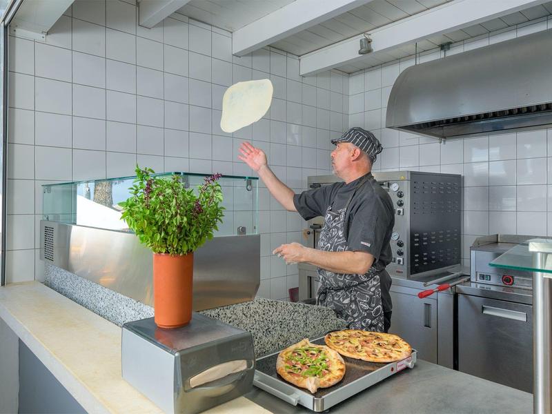 Cuoco lancia l'impasto per pizza in una cucina all'aperto moderna in una giornata di sole.