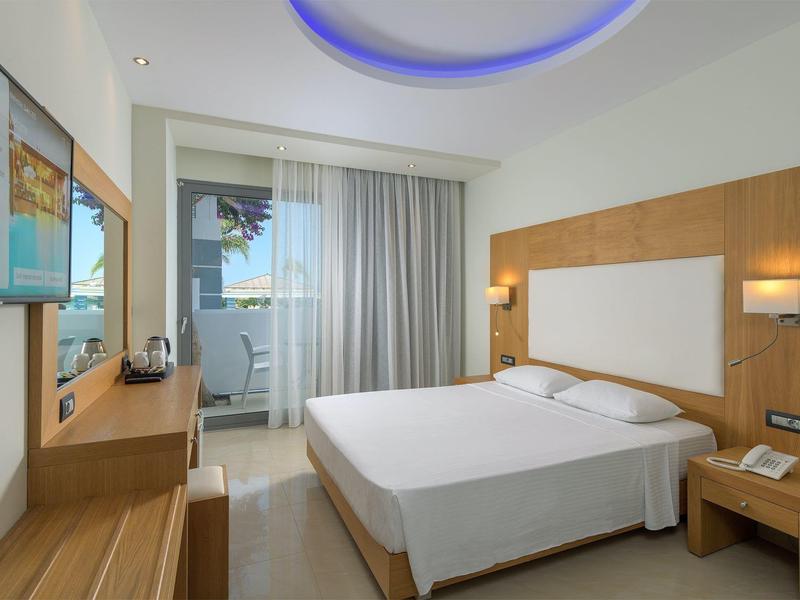 Camera d'hotel moderna con letto matrimoniale, pannelli in legno e balcone con vista sulla piscina.