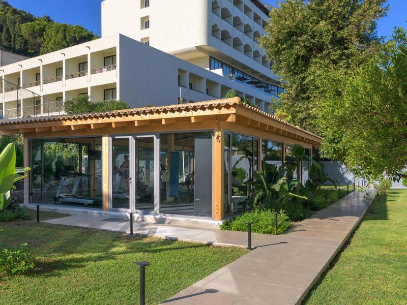 Edificio di hotel moderno con veranda in vetro e giardino in una giornata di sole.