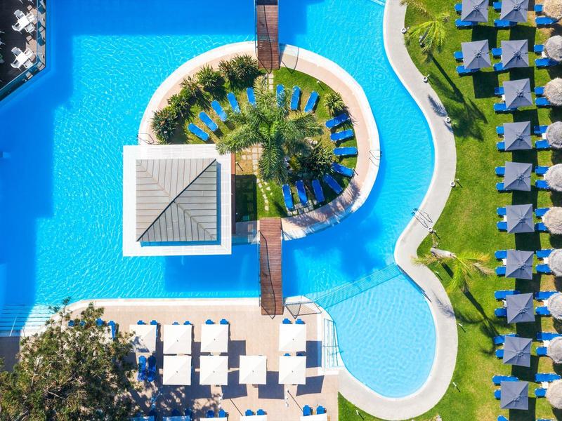 Vista aerea di una piscina con lettini e ombrelloni in un resort alberghiero.