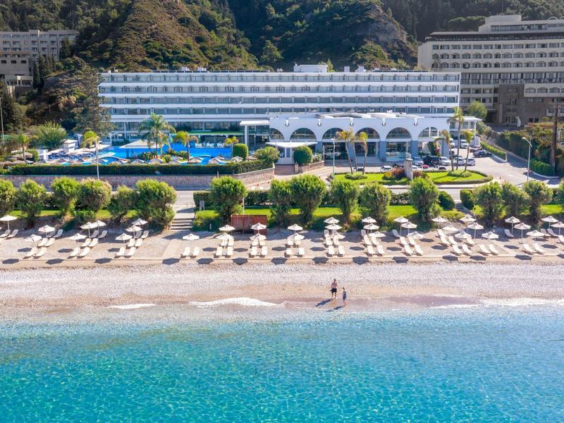 Grande hotel con piscina e ombrelloni sulla spiaggia di fronte all'acqua azzurra.