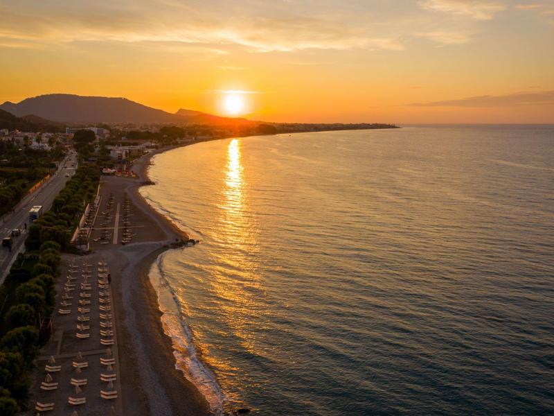 Tramonto su una spiaggia calma con acqua tranquilla e montagne sullo sfondo.