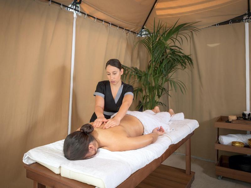 Donna che fa un massaggio a un uomo su un lettino in una tenda con piante.