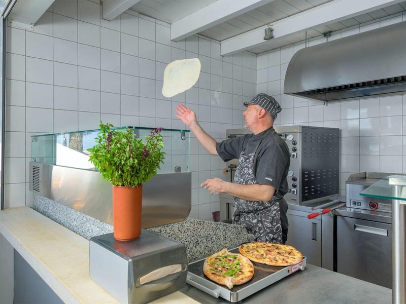 Cuoco lancia l'impasto della pizza in una cucina d'hotel moderna con grill e forno per pizza.