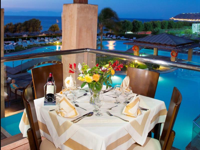 Tavolo romantico apparecchiato con fiori, vino e vista mare al tramonto.