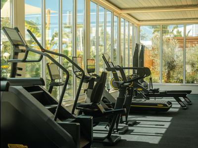 Attrezzature fitness moderne in una palestra luminosa e spaziosa con grandi finestre che affacciano sul verde.