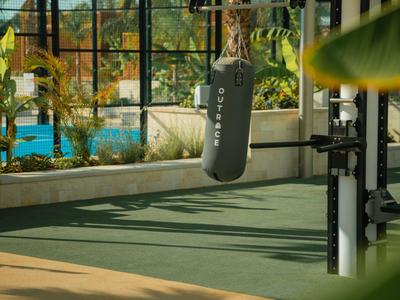 Area allenamento con sacco da boxe e attrezzi fitness accanto a piscina e palme.