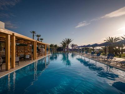 Piscina all'aperto sul mare con palme e ombrelloni al tramonto.