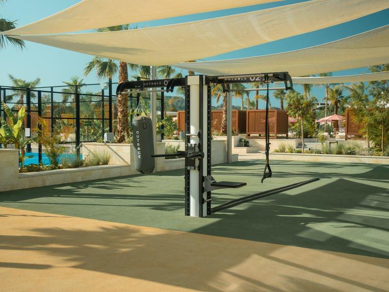 Area sportiva esterna coperta con attrezzature e palme sullo sfondo.