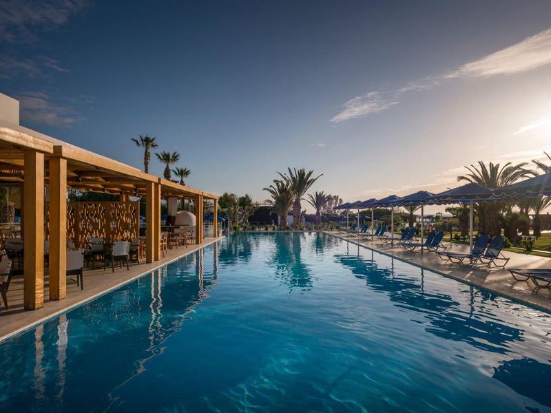 Piscina all'aperto sul mare con palme e ombrelloni al tramonto.
