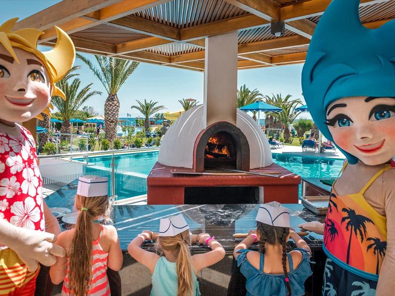 Bambini giocano vicino a una piscina con un forno per pizza all'aperto e maschere colorate.