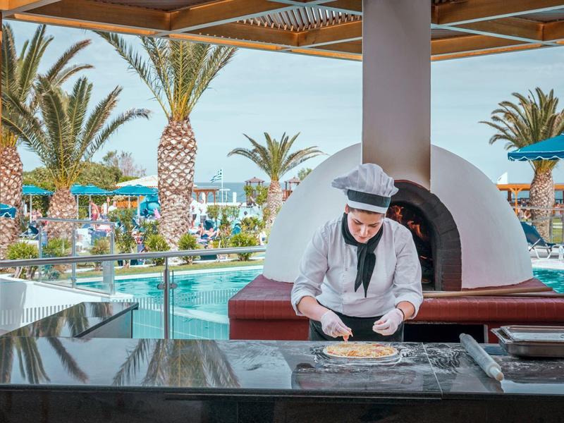 Chef in divisa che prepara l'impasto vicino alla piscina e alle palme sotto un tetto.