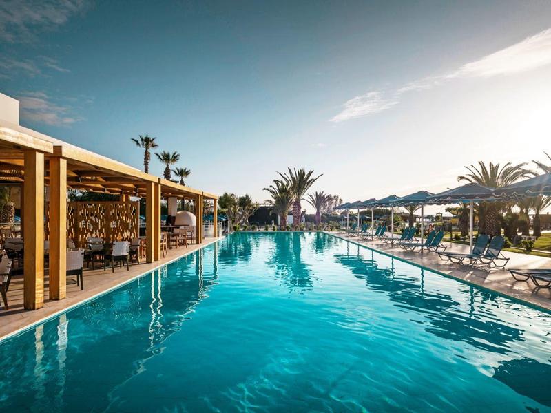 Piscina all'aperto di un hotel con palme e lettini al tramonto.