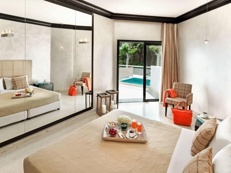 Camera d'hotel moderna con letto, specchio a parete, poltrona e vista sulla piscina.