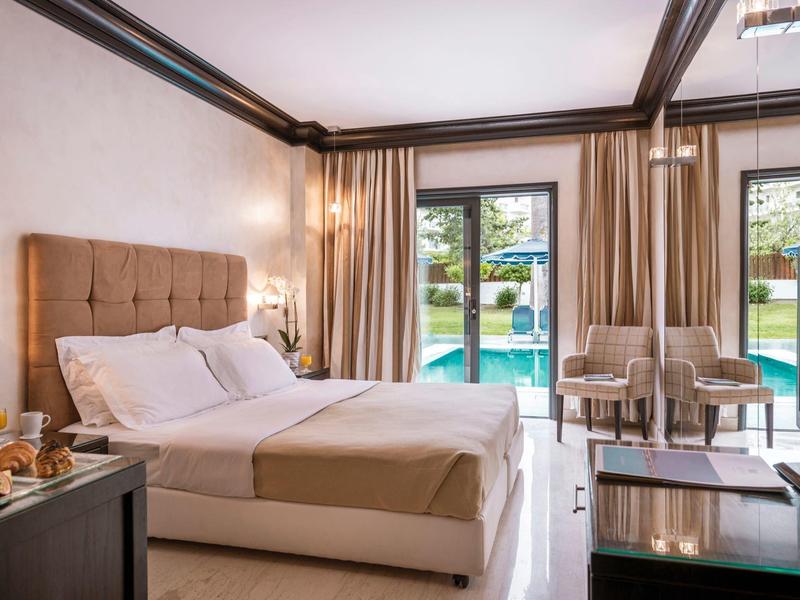 Camera d'hotel luminosa con letto matrimoniale, terrazza e piscina visibile all'esterno.