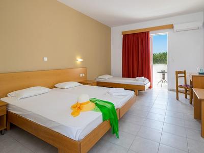 Bright hotel room with two beds, desk, TV, and balcony with red curtain.