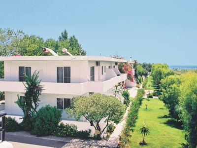Modernes, weißes Gebäude mit Balkon, umgeben von grünem Garten und Blick aufs Meer.