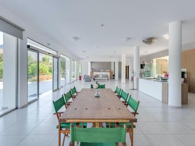 Großer heller Essbereich mit langem Holztisch und grünen Stühlen, große Fenster bieten Aussicht.