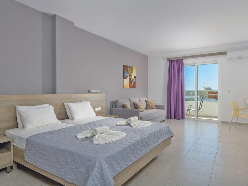 Bright hotel room with double bed, seating area, and balcony with sea view.