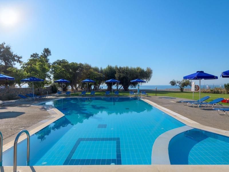 Large outdoor pool with blue umbrellas and sea view under clear sky.
