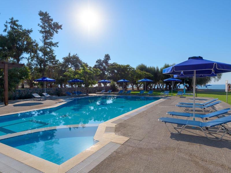 Sunny hotel pool area with blue umbrellas and lounge chairs under a clear sky.