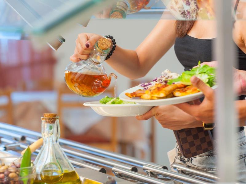 Person pouring sauce over roasted potatoes on a plate in buffet restaurant