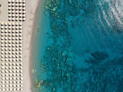 Vista aérea de una playa con filas de sombrillas junto a agua azul clara.