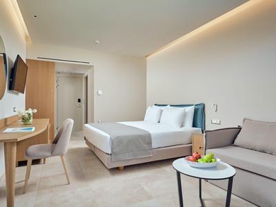 Habitación de hotel luminosa con cama doble, sofá, escritorio y espejos redondos en la pared.