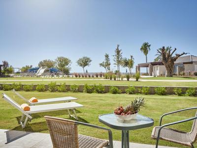 Garten mit grünem Rasen, Terassentisch mit Obstschale, zwei Stühlen und Liegestühlen im Hintergrund.