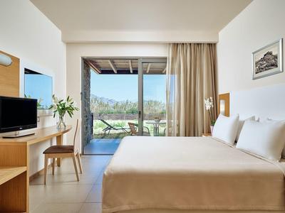 Habitación de hotel luminosa con cama doble, TV, escritorio y vista a terraza y paisaje.