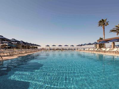 Grand piscine extérieure avec chaises longues et parasols sous un ciel clair.