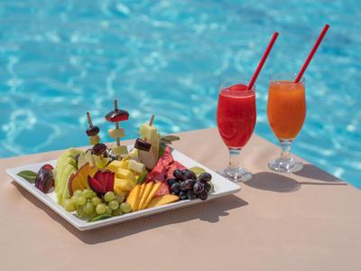 Plateau de fruits coloré et deux cocktails vibrants à côté d'une piscine.