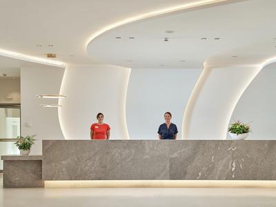 Nowoczesna recepcja hotelowa z dwoma pracownikami za szarym kamiennym biurkiem i minimalistycznym designem.