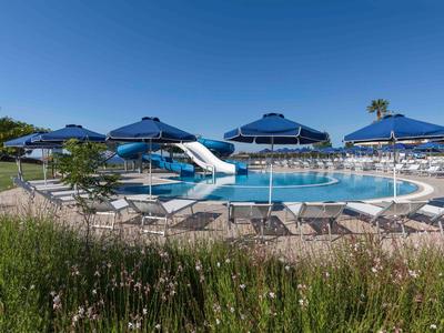 Espace piscine avec toboggan, chaises longues et parasols bleus sous un ciel clair.