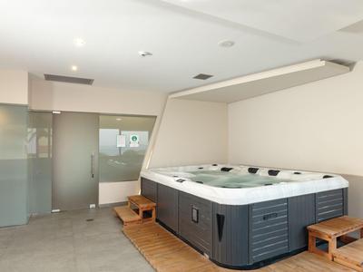 Nowoczesna strefa wellness z dużym jacuzzi i drewnianymi ławkami w jasnym pomieszczeniu.