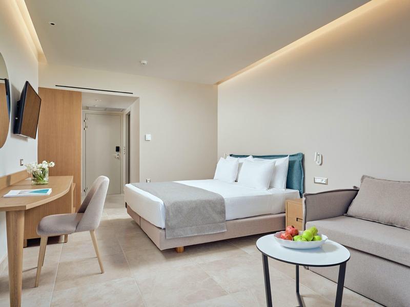 Habitación de hotel luminosa con cama doble, sofá, escritorio y espejos redondos en la pared.