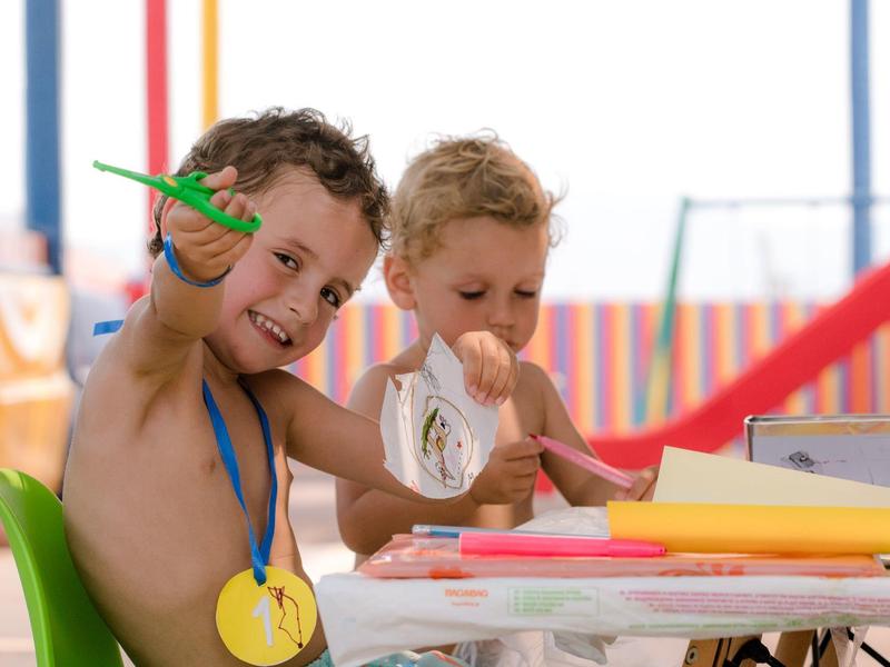 Dos niños están sentados en la mesa haciendo manualidades con papel de colores en un área de juegos luminosa.