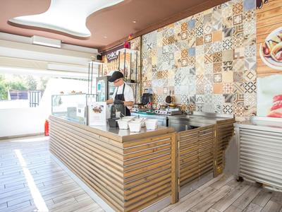 Modern kiosk with wooden counter and colorful tiled wall, open to a sunny outdoor area.
