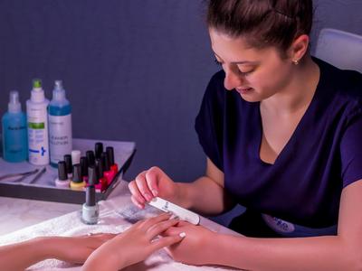 Woman receiving manicure, nail care with various polishes and care products in the background.