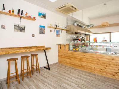 Bright café with wooden counter, three bar stools, and wall shelves with decorations.