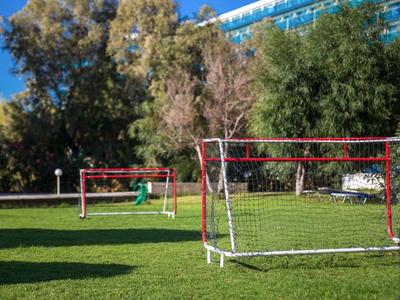 Dwie małe bramki do piłki nożnej na trawniku przed budynkiem hotelu i drzewami