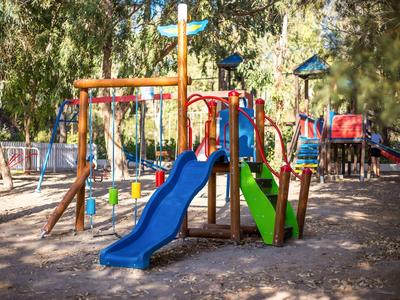 Colorful children's playground with slides and climbing equipment outdoors under trees.