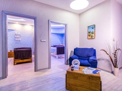 Modern furnished hotel waiting area with sofa, wooden table, and view into two rooms.