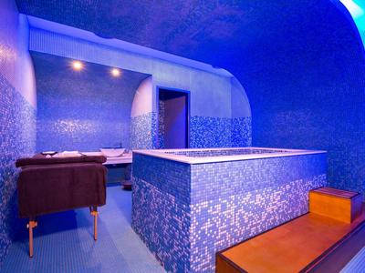 Bright spa with blue tiled bathtub, lounge chairs, and ambient lighting.