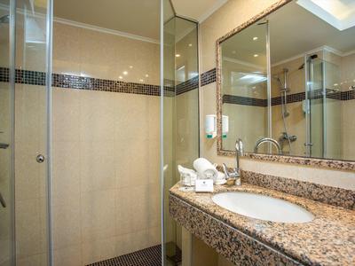 Bright hotel shower with glass enclosure and sink on marble countertop.
