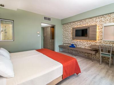 Modern hotel room with large bed, red throw, and desk by the window.