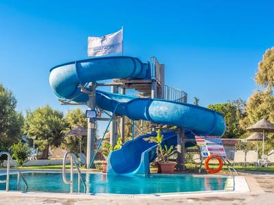 Water slide at an outdoor pool with sun umbrellas and trees in the background.